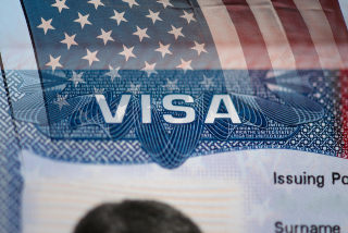 Imagem de um visto americano com parte da bandeira dos Estados Unidos ao fundo.